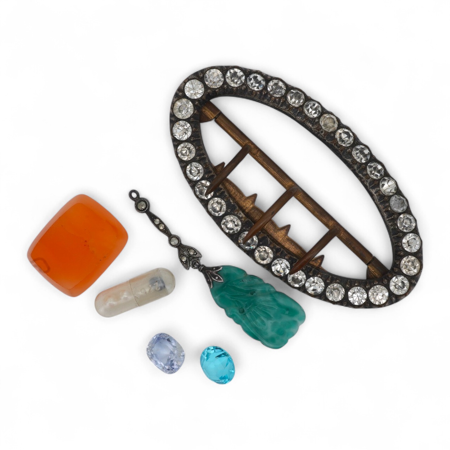 A collection of jewels and a loose sapphire, comprising: a shoe buckle set with colourless pastes, length 6.8cm; a green paste and marcasite pendant imitating jadeite; a polished slab of carnelian; a loose cushion-shaped